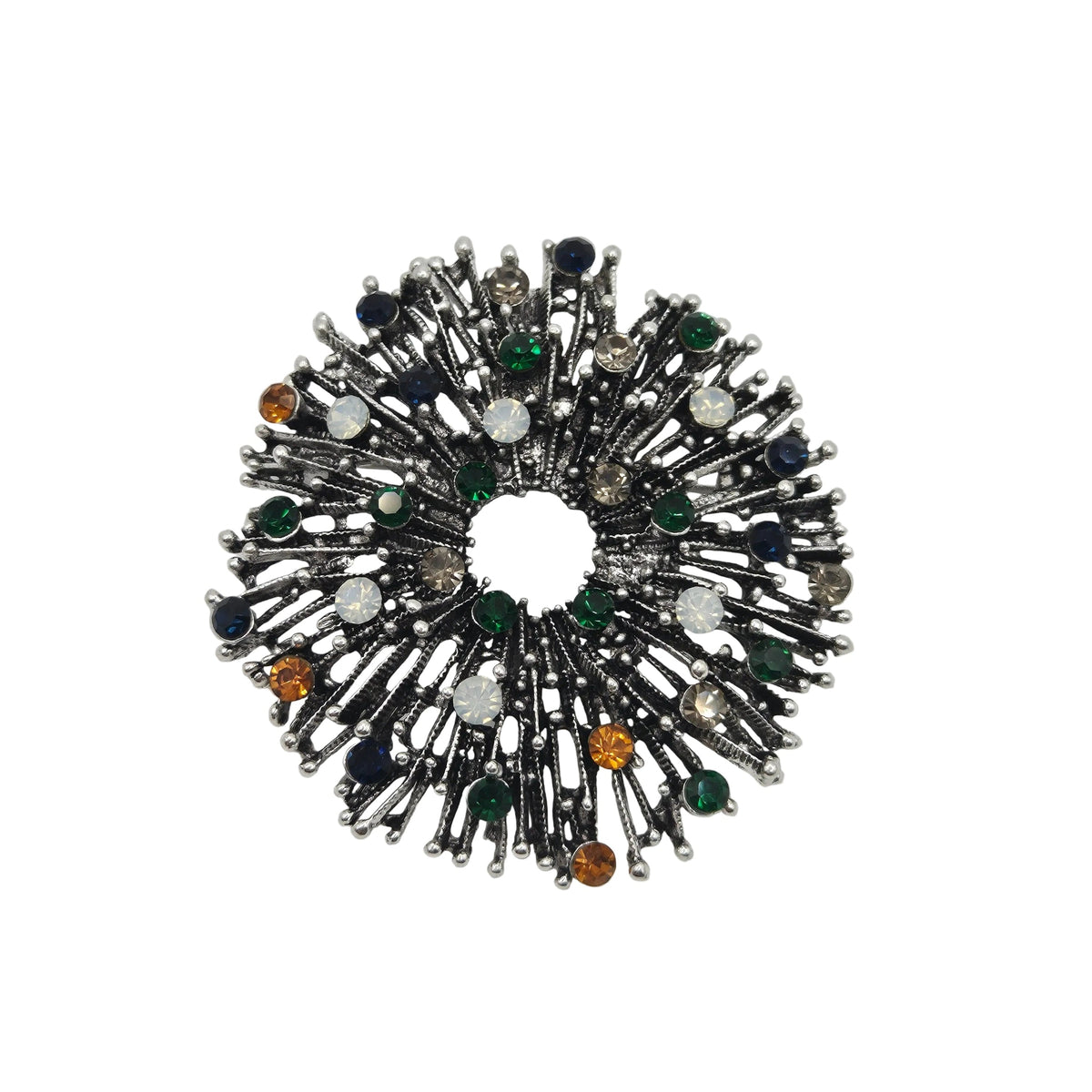 A circular firework brooch with an antique silver-toned design, embellished with dark blue, green, and amber faceted gemstones, set against a plain white background.
