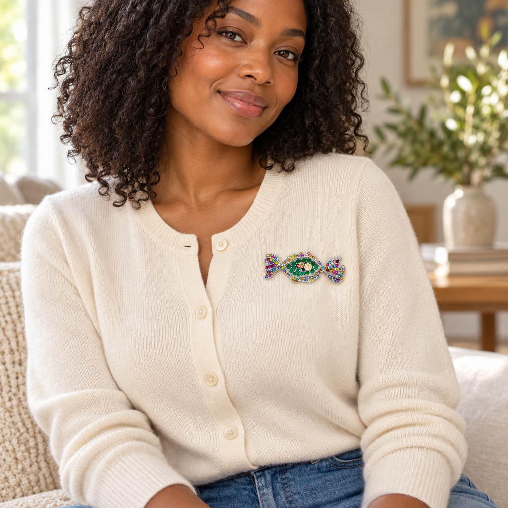 Woman wearing a multicoloured rhinestone candy brooch with green centre stones and a silver tone setting on a cream cardigan, styled with blue jeans.