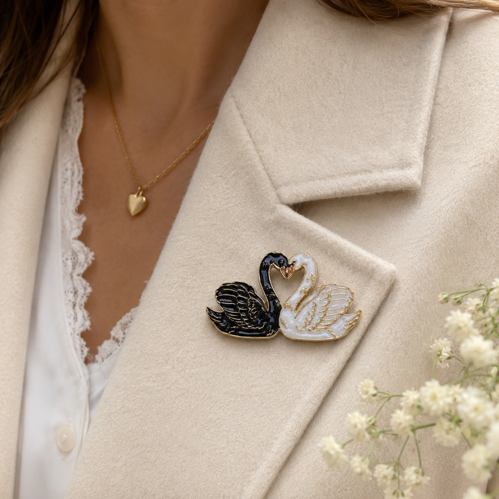 A close-up of a person wearing a cream-colored blazer over a white lace-trim blouse, with a gold heart necklace and a black-and-white swan lapel pin. Small white flowers are tucked into the blazer.