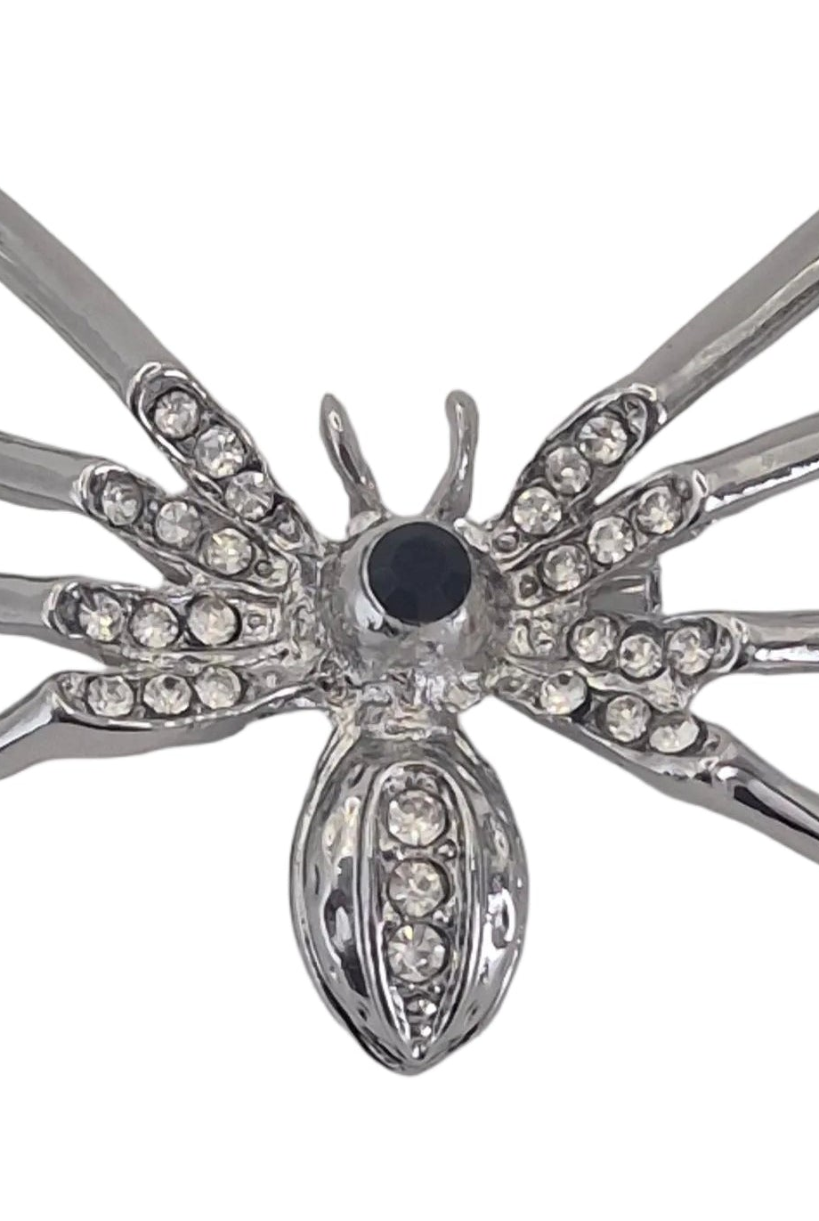 A silver spider brooch decorated with clear rhinestones on its legs and abdomen, featuring a central round black stone, shown against a plain white background.
