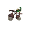 An acorn brooch featuring two brown textured acorns covered in clear rhinestones, attached to a branch with a glossy green leaf, shown on a plain white background.