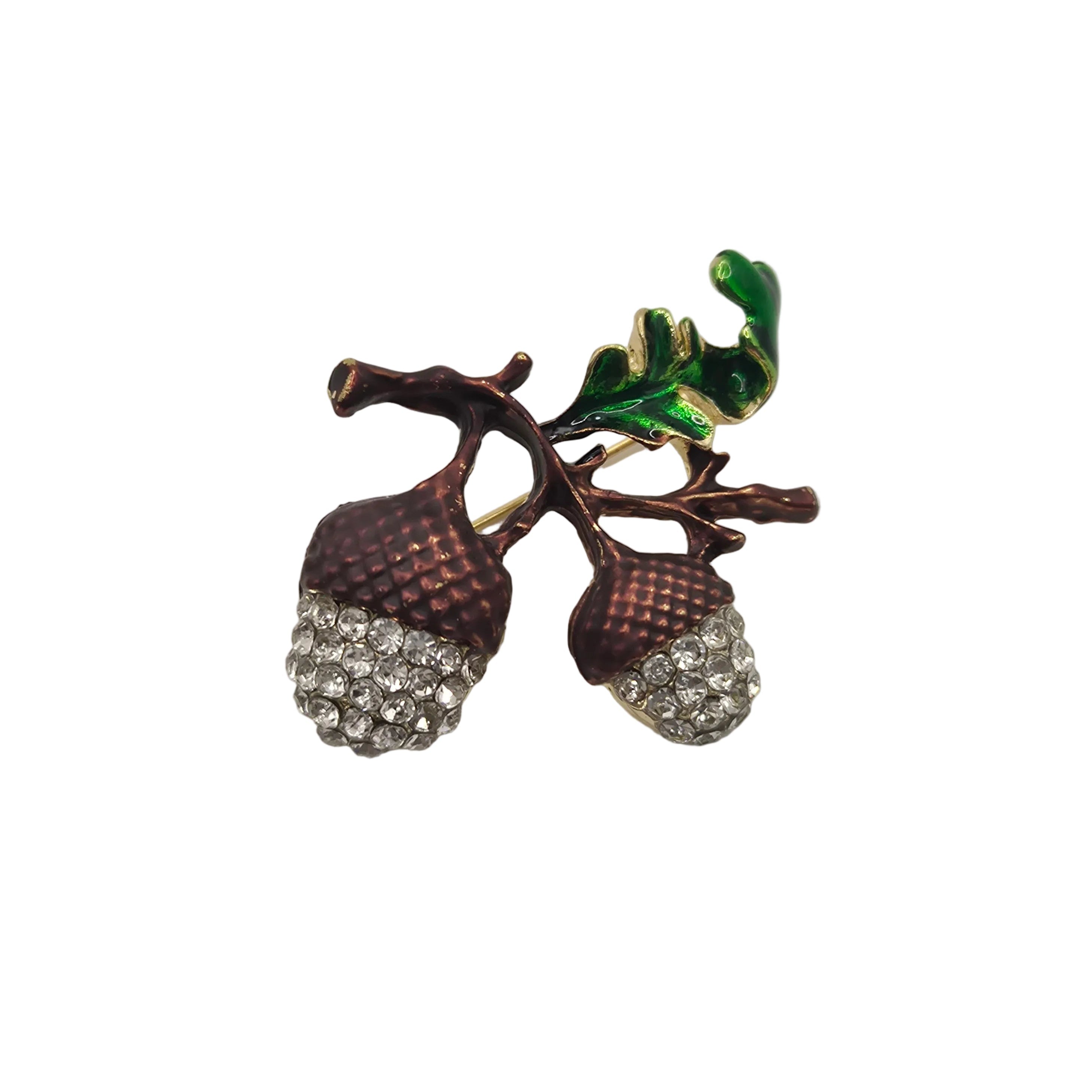An acorn brooch featuring two brown textured acorns covered in clear rhinestones, attached to a branch with a glossy green leaf, shown on a plain white background.