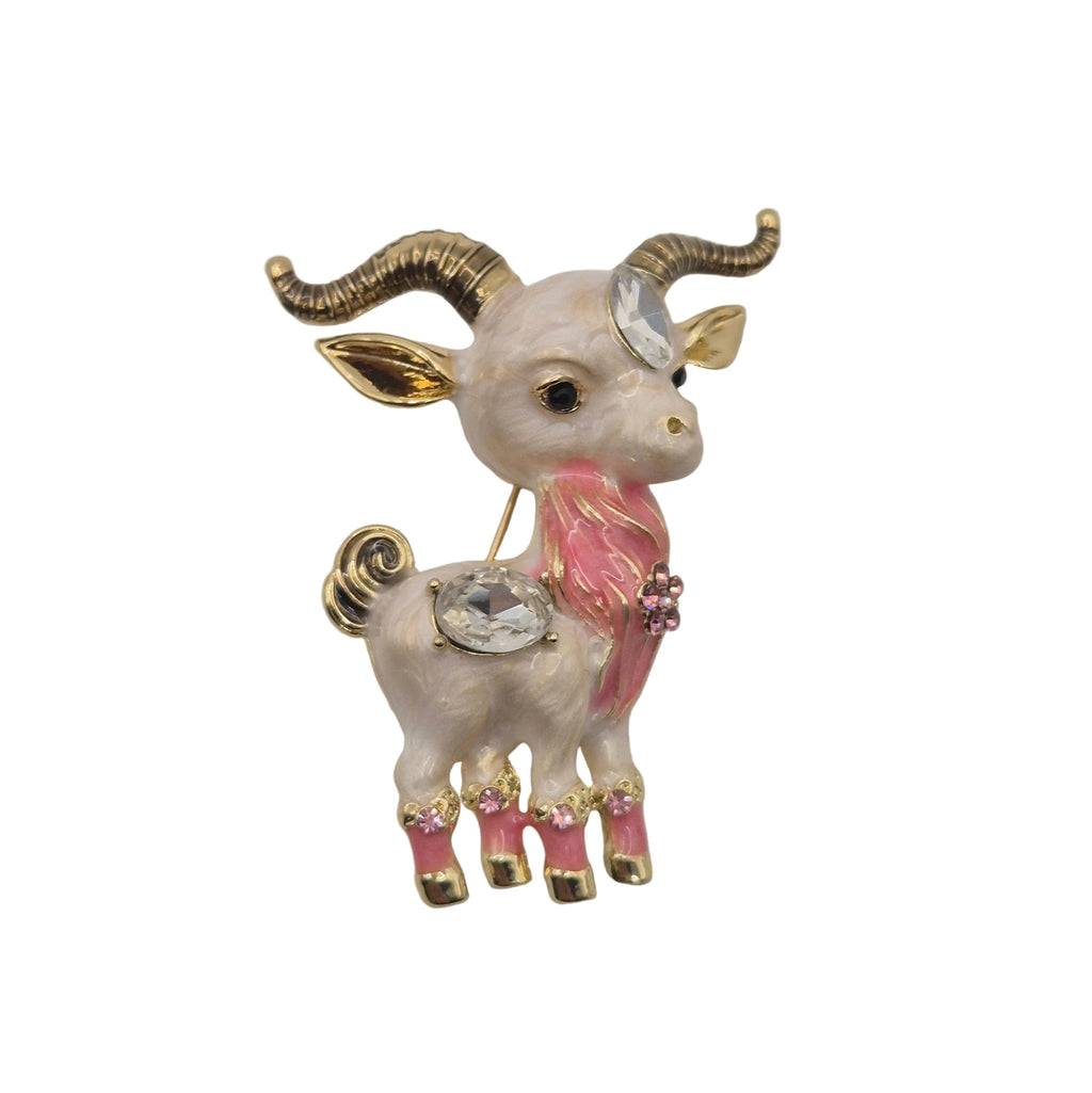 A decorative ram brooch with gold-toned horns and legs, a pink neck and tail accents, and a clear rhinestone on its forehead, shown on a plain white background.