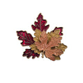 An autumn maple leaf brooch featuring three layered leaves in burgundy red, metallic gold, and copper/rose gold, outlined with gold-tone metal borders, set against a plain white background.