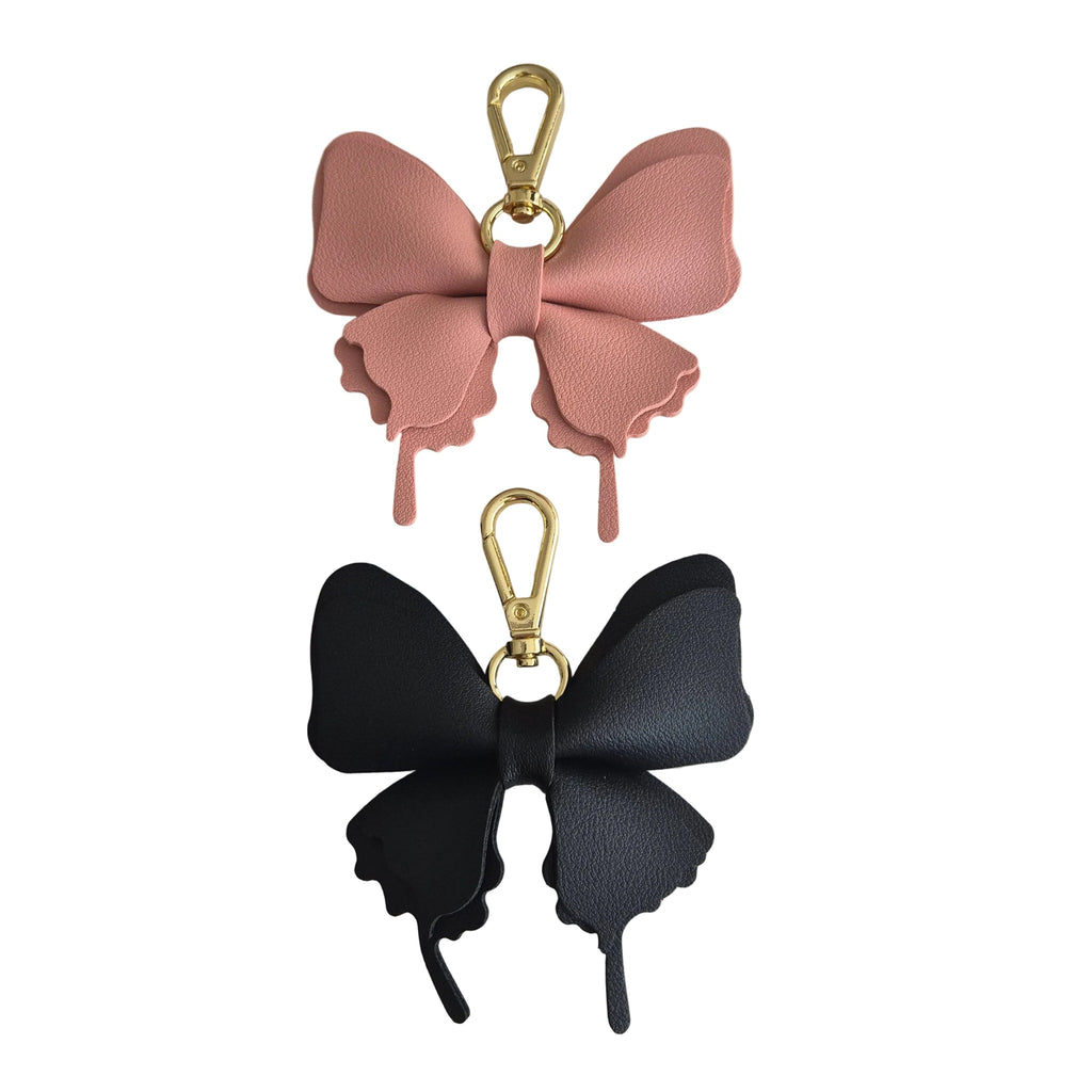 Two butterfly-shaped bag charms or keychains with gold-tone clasp hardware, one in dusty pink and one in black, displayed on a plain white background.