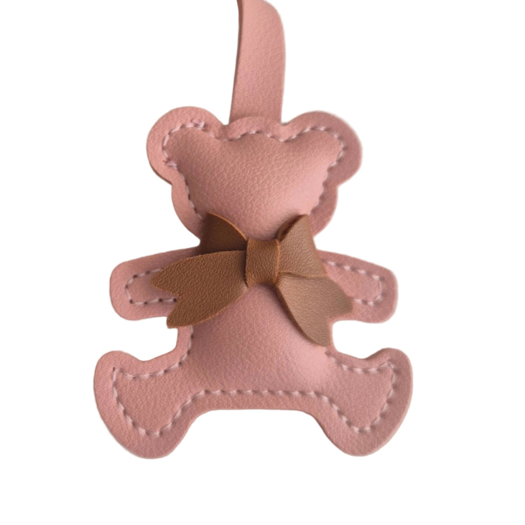 A pink faux leather teddy bear bag charm with a brown bow and a pink hanging loop, shown on a plain white background.