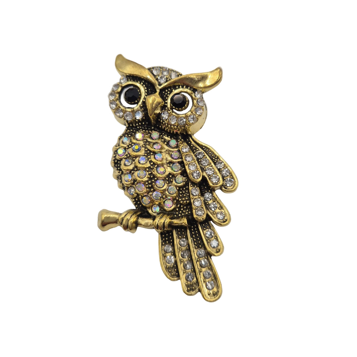 Gold owl brooch embellished with clear rhinestones, resting on a small branch, set against a plain white background.