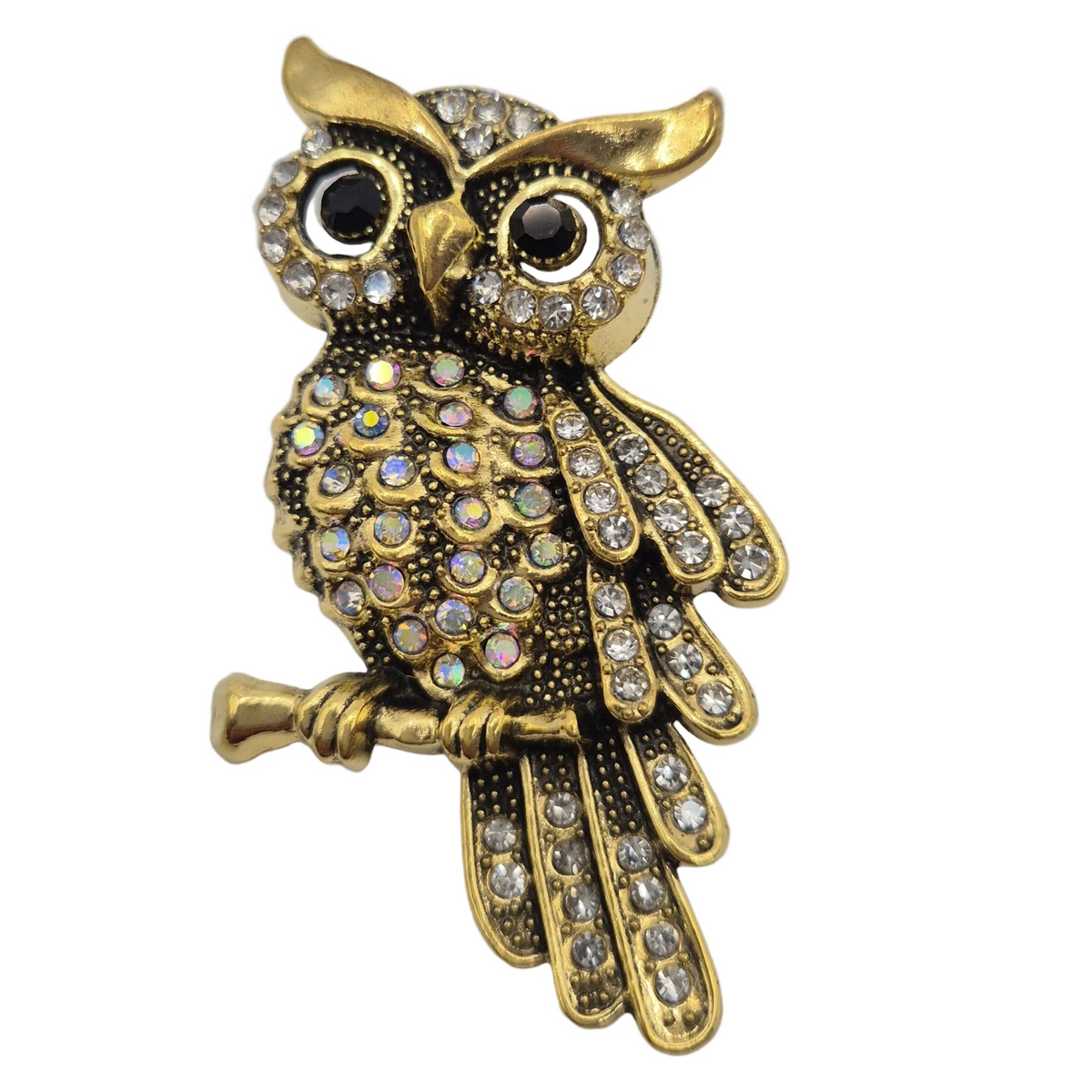 Gold owl brooch embellished with clear rhinestones and black stone eyes, perched on a branch against a white background.