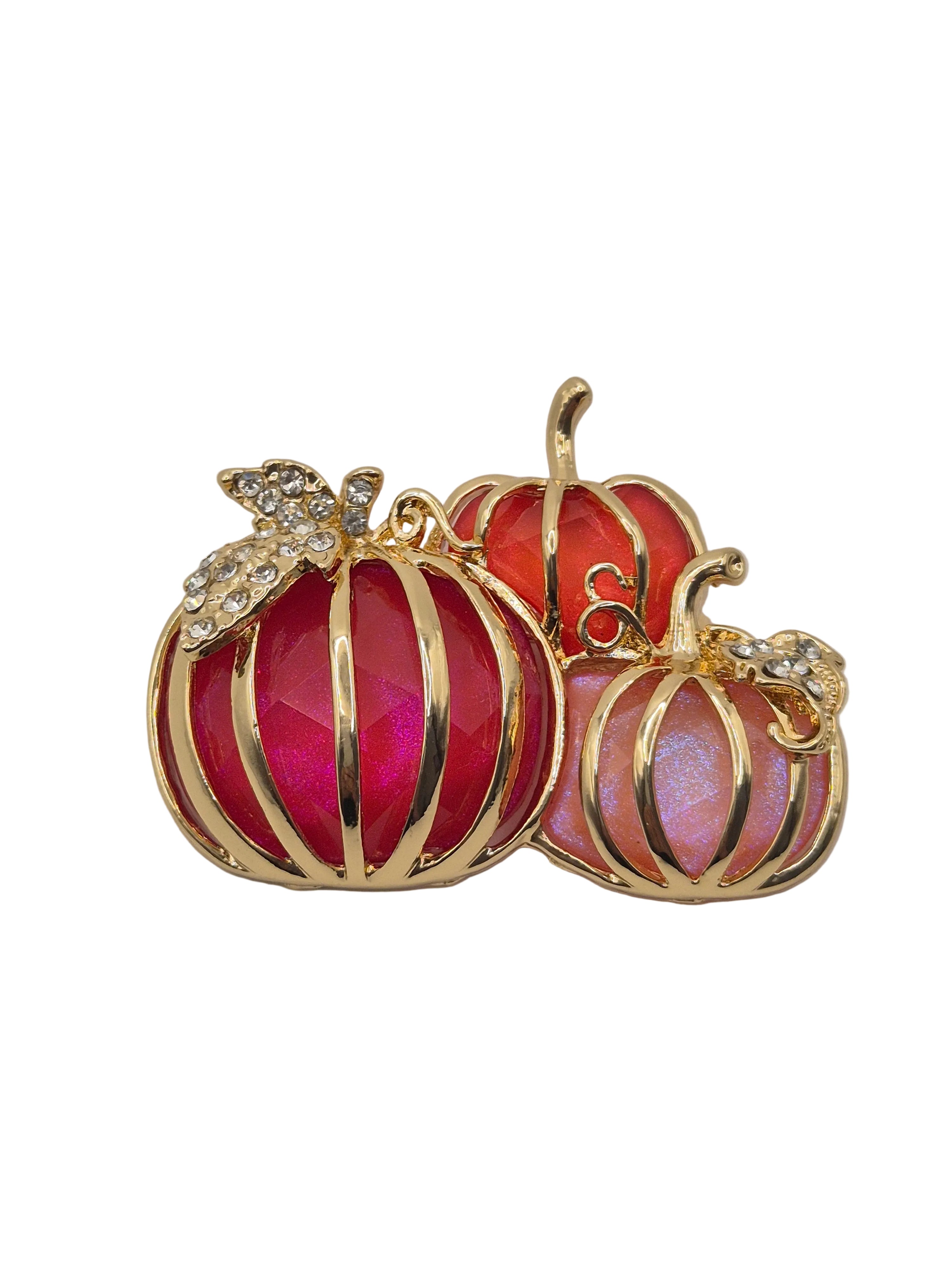 A gold-toned brooch featuring three pumpkin shapes with faceted pink and red enamel, accented with small clear rhinestones on the stems and tops.