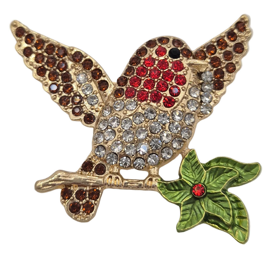 A gold tone robin bird brooch with wings spread, embellished with red and brown rhinestones, perched on a green leafy branch with a small red jewel accent, shown on a plain white background.