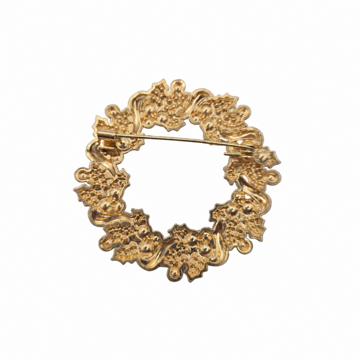 A gold-tone circular brooch with an ornate, textured floral and scroll pattern, featuring a visible pin mechanism on the back, set against a plain white background.