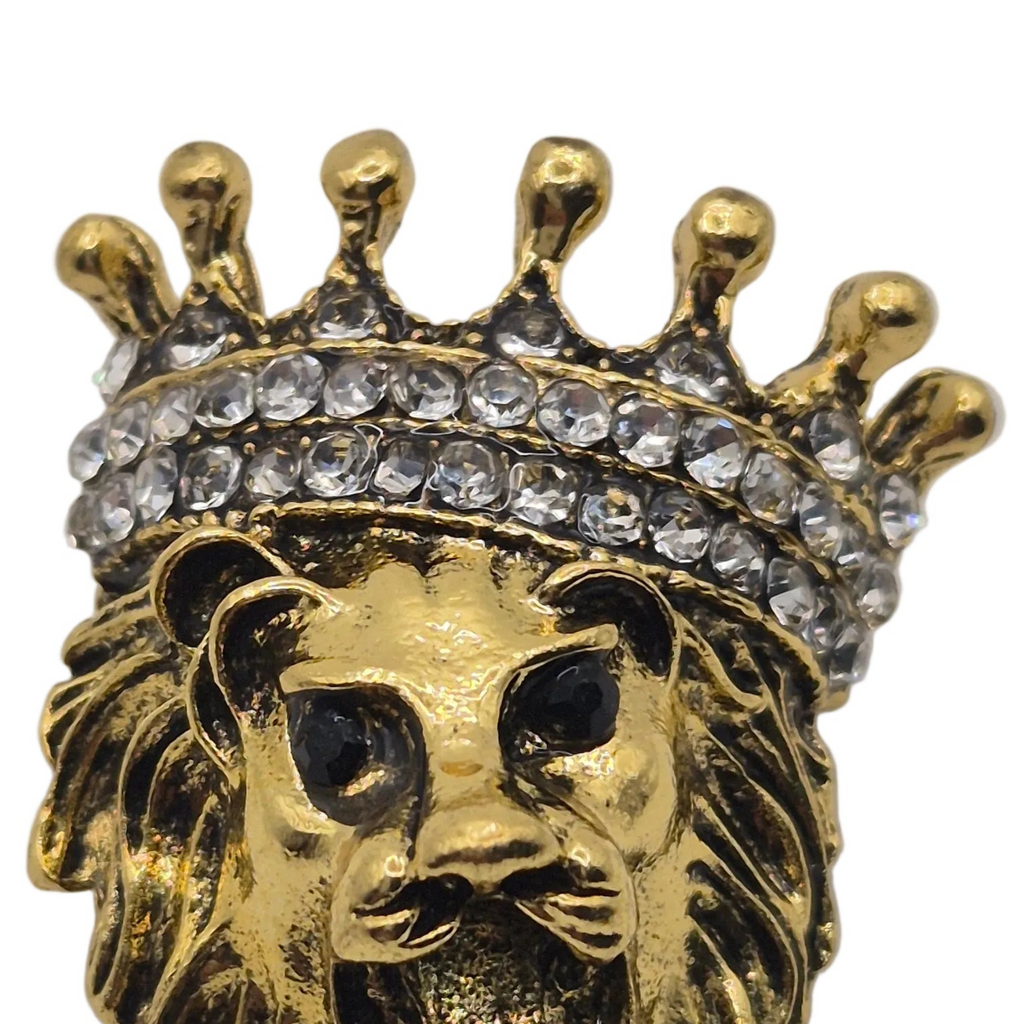 Gold lion head jewelry piece wearing a jeweled crown, shown in a close-up product shot against a white background.
