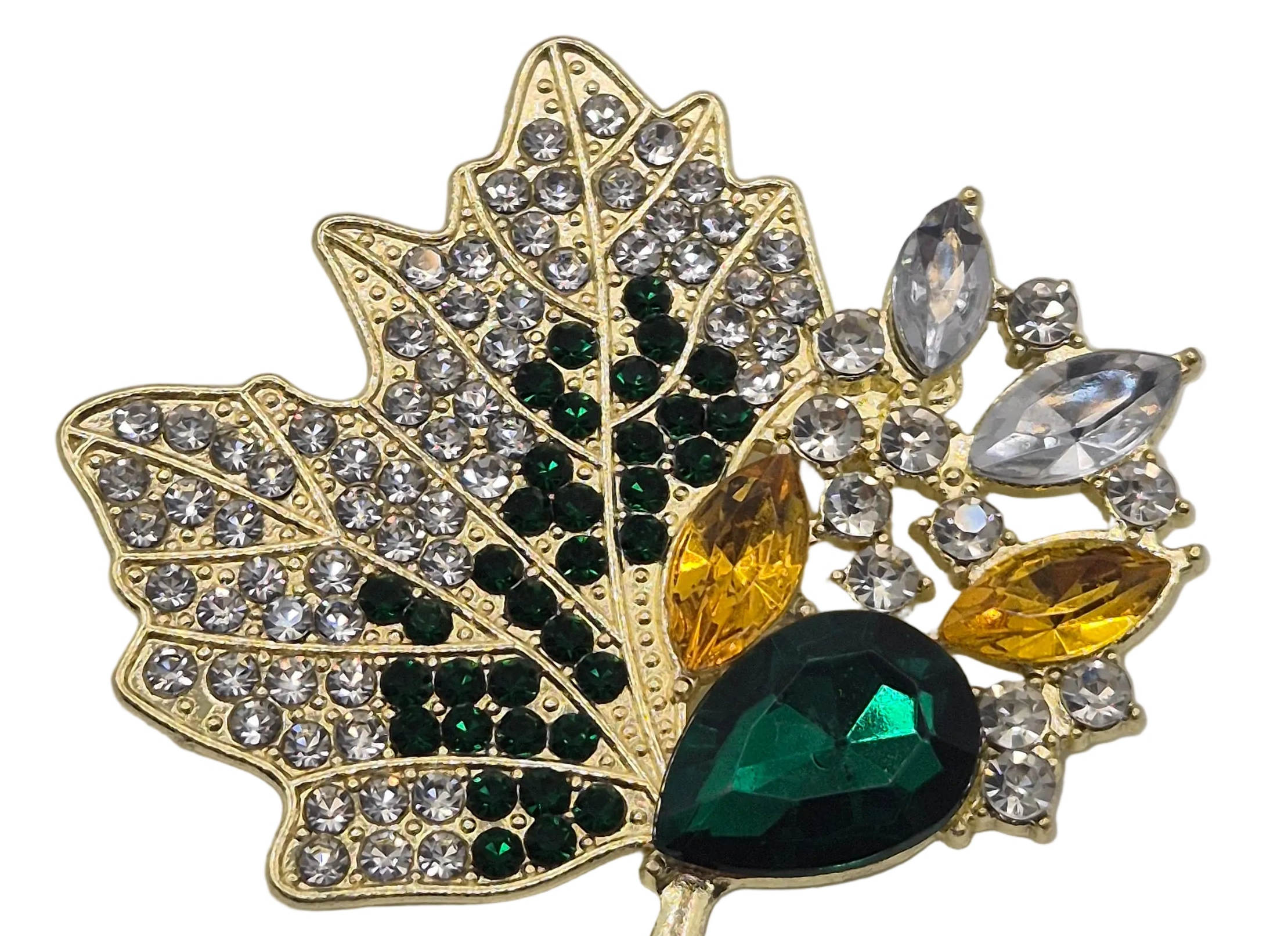 A gold-toned maple leaf brooch embellished with clear rhinestones, dark green round stones, yellow marquise stones, and a large faceted dark green teardrop crystal, shown on a plain white background.