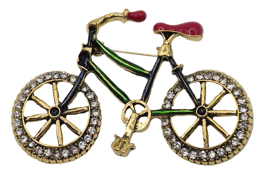 A bicycle-shaped brooch featuring gold-tone metal with black, green, and red enamel details, and clear rhinestone-studded wheels, shown on a plain white background.