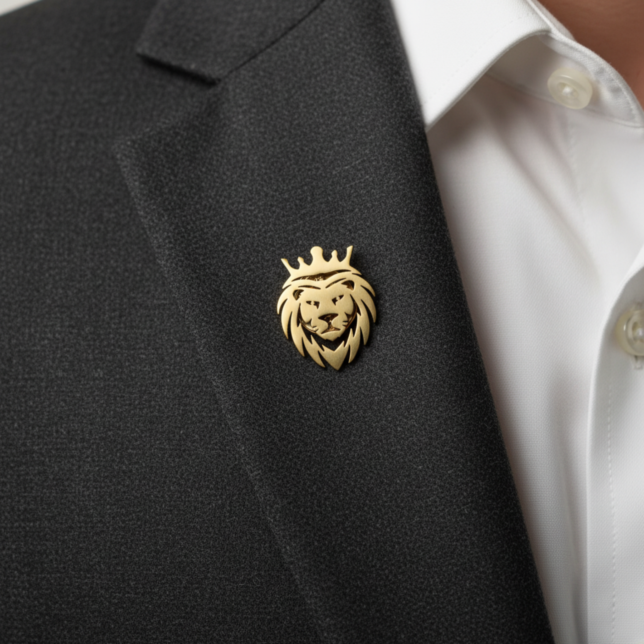 A gold lion head with a crown lapel pin worn on a black blazer over a white collared shirt.