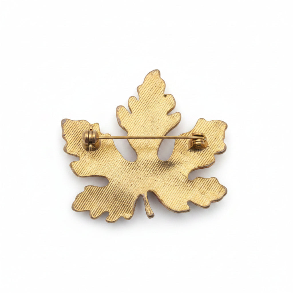 A gold-toned metal leaf-shaped brooch with a textured surface and a pin wire visible on the reverse side, shown against a plain white background.