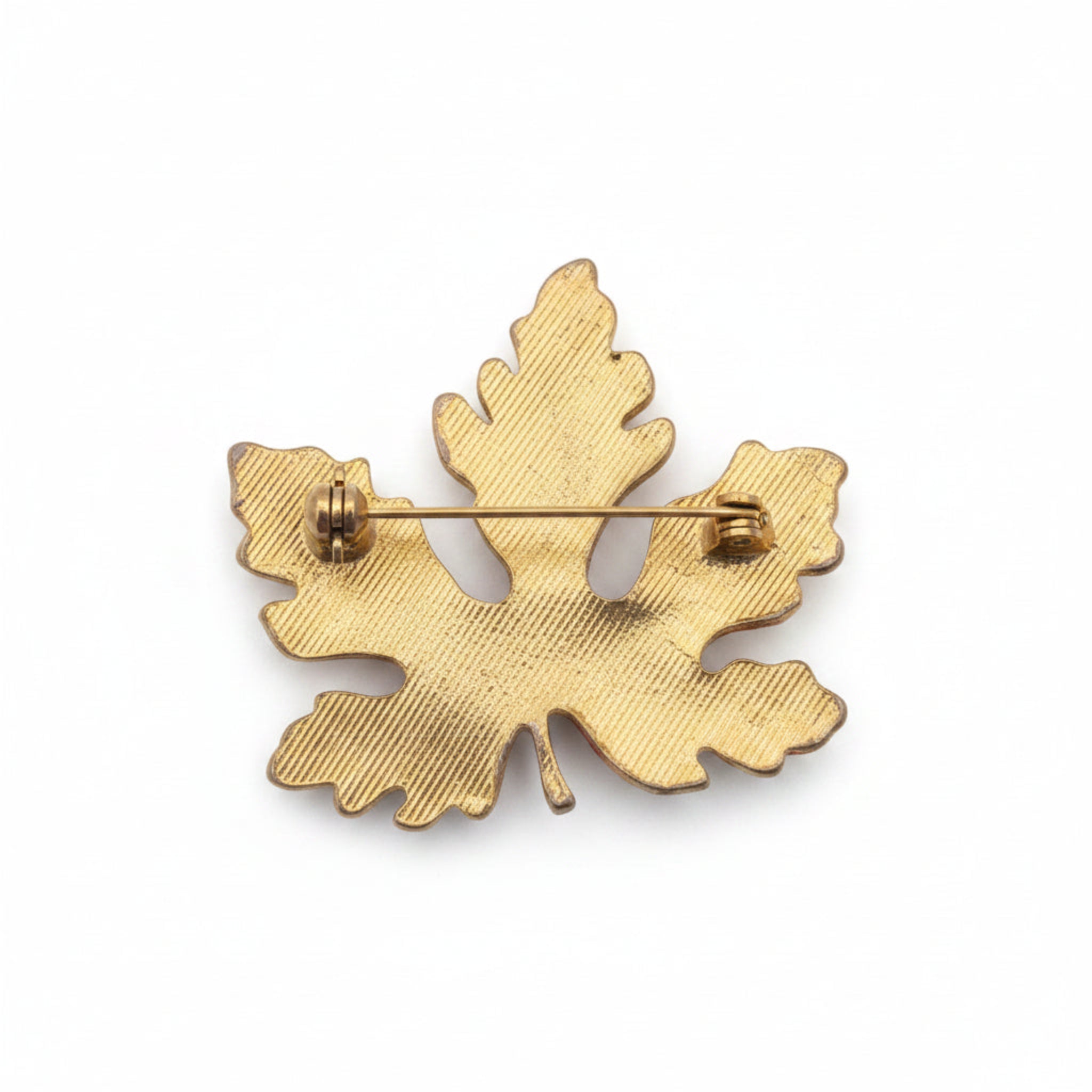 A gold-toned metal leaf-shaped brooch with a textured surface and a pin wire visible on the reverse side, shown against a plain white background.