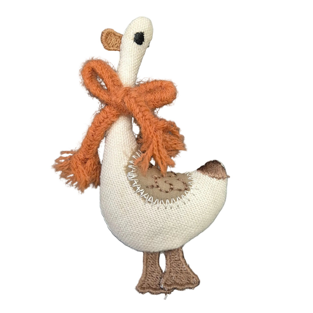 A fabric goose brooch pin with a cream-colored body, orange scarf, and brown accents, isolated on a plain white background.