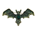 A vintage bat-shaped brooch featuring green enamel wings and body with gold-tone metal outlines and rhinestone accents, displayed on a neutral white background.