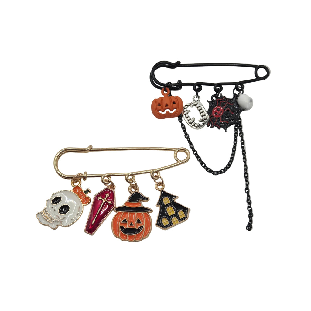 Two Halloween-themed safety pins brooches displayed on a white background. The top safety pin is black with orange, silver, and red charms including a jack-o'-lantern, spider, and skull.