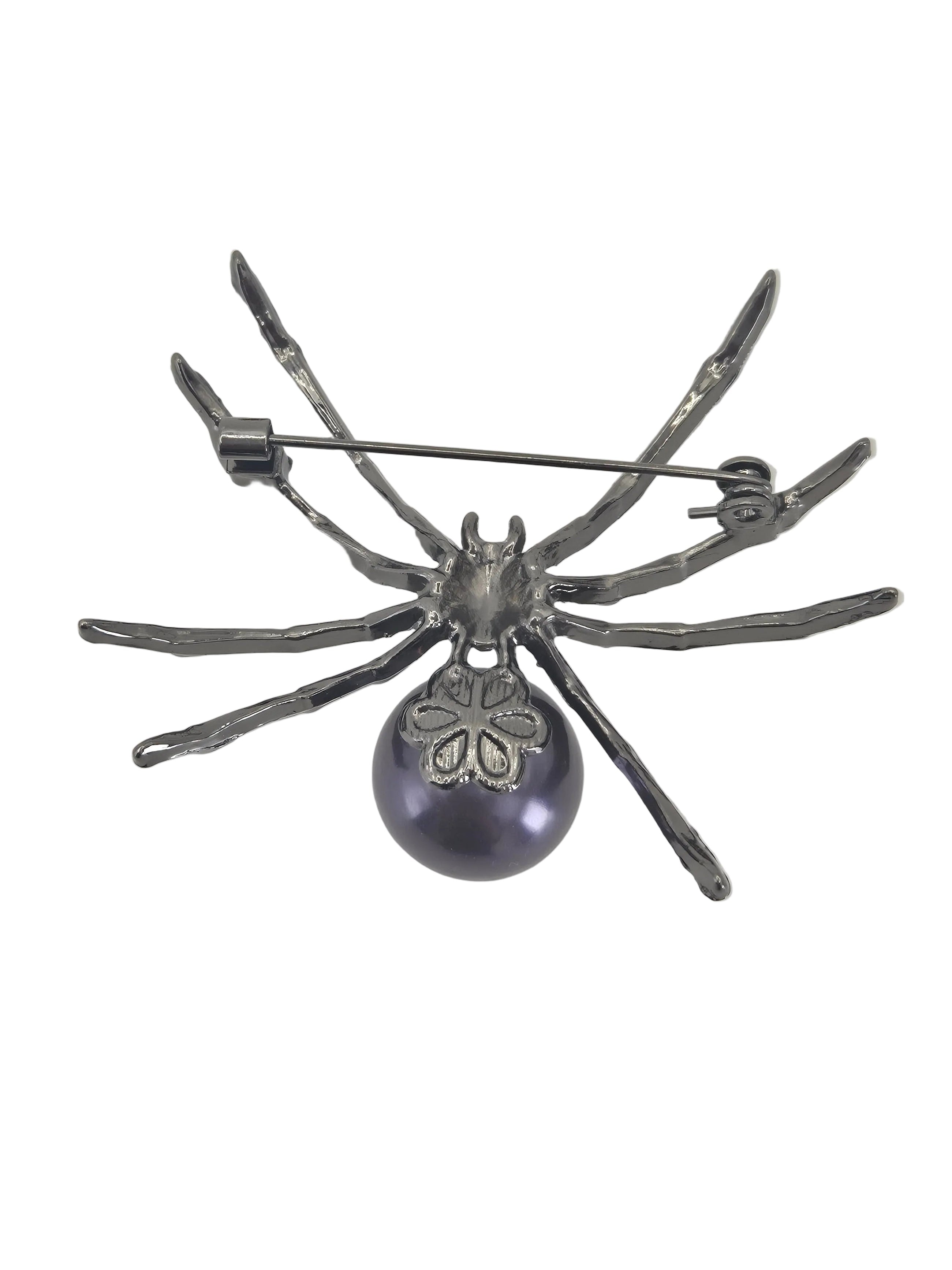 A spider-shaped brooch with metallic silver legs and a dark purple round pearl pendant, shown against a plain white background.