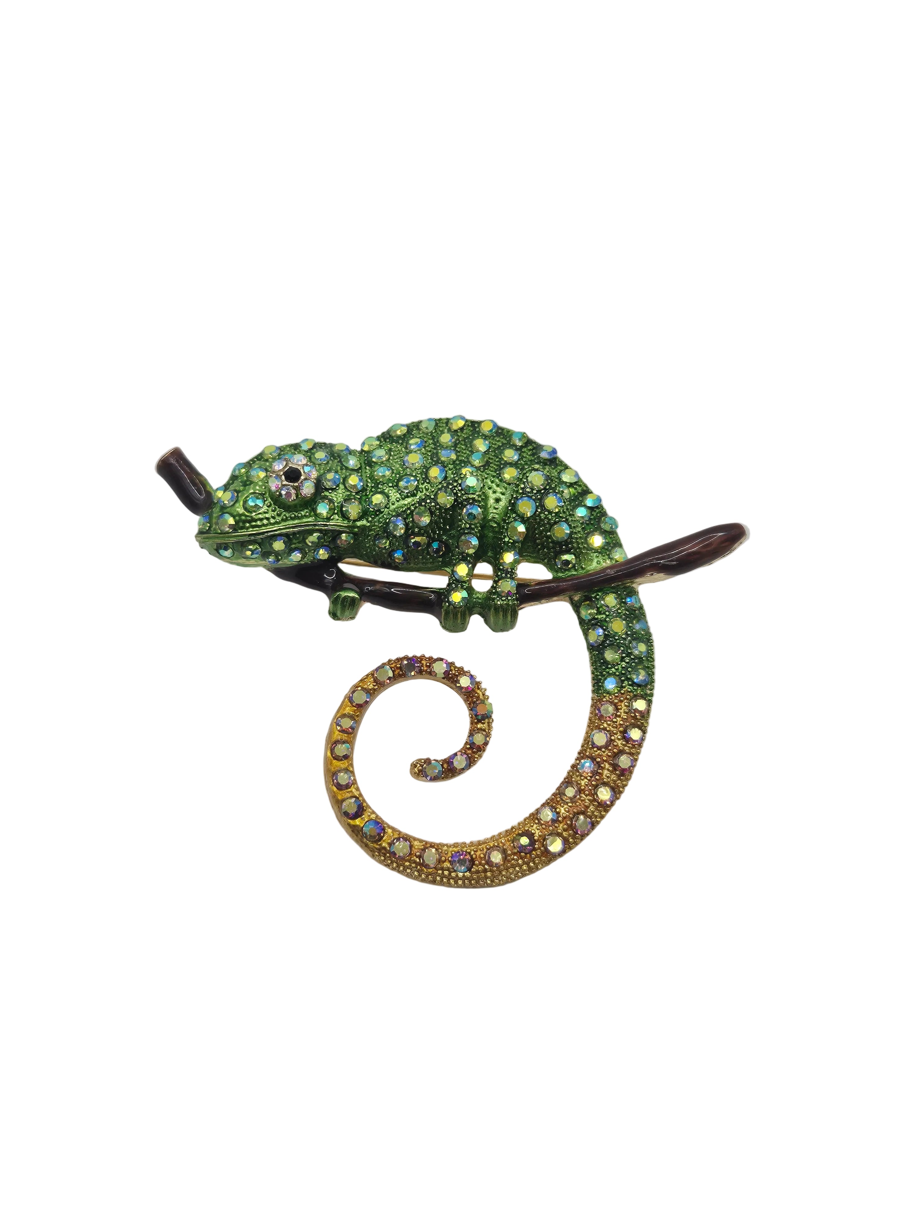 A green chameleon brooch embellished with iridescent green and gold rhinestones, perched on a dark brown branch against a white background.