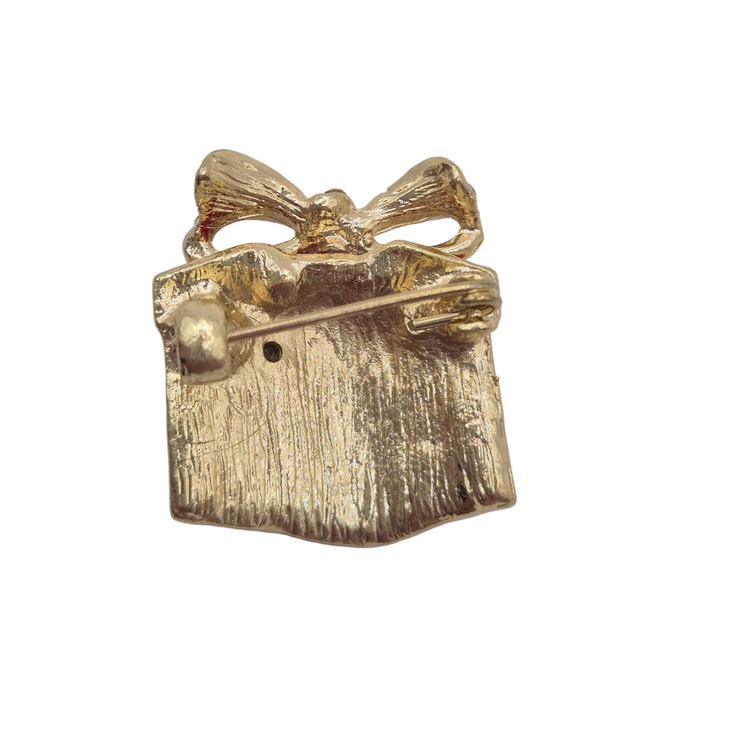 A small gold gift box brooch with a textured finish and ribbon detail, photographed on a plain white background.