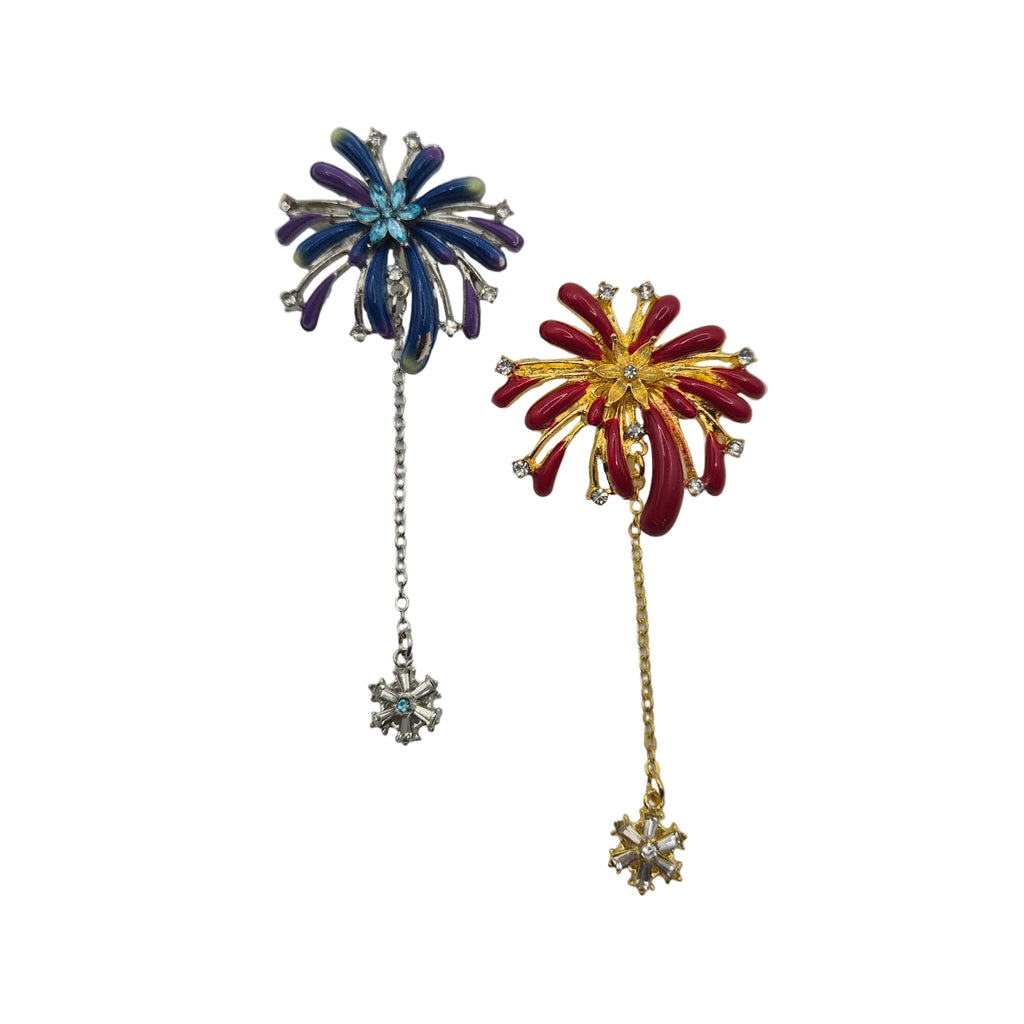 Two vintage-style firework brooch pins on a plain white background. One brooch is blue and purple with a silver-tone chain and star pendant. The other is red and yellow with star pendant.