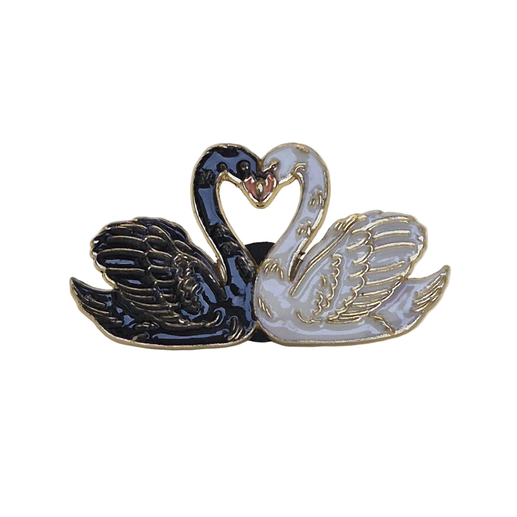 A twin swan enamel lapel pin featuring one black swan and one white swan facing each other to form a heart shape with their necks, outlined in gold-tone metal.