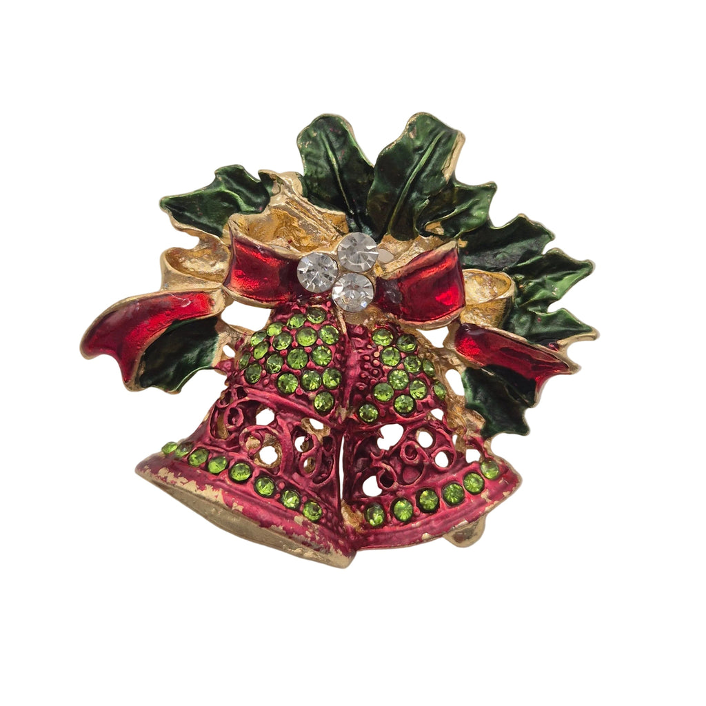 A Christmas-themed brooch featuring two gold-tone bell-shaped ornaments decorated with pink and green enamel, topped with a red bow, green holly leaves, and a clear rhinestone center, shown on a plain white background.