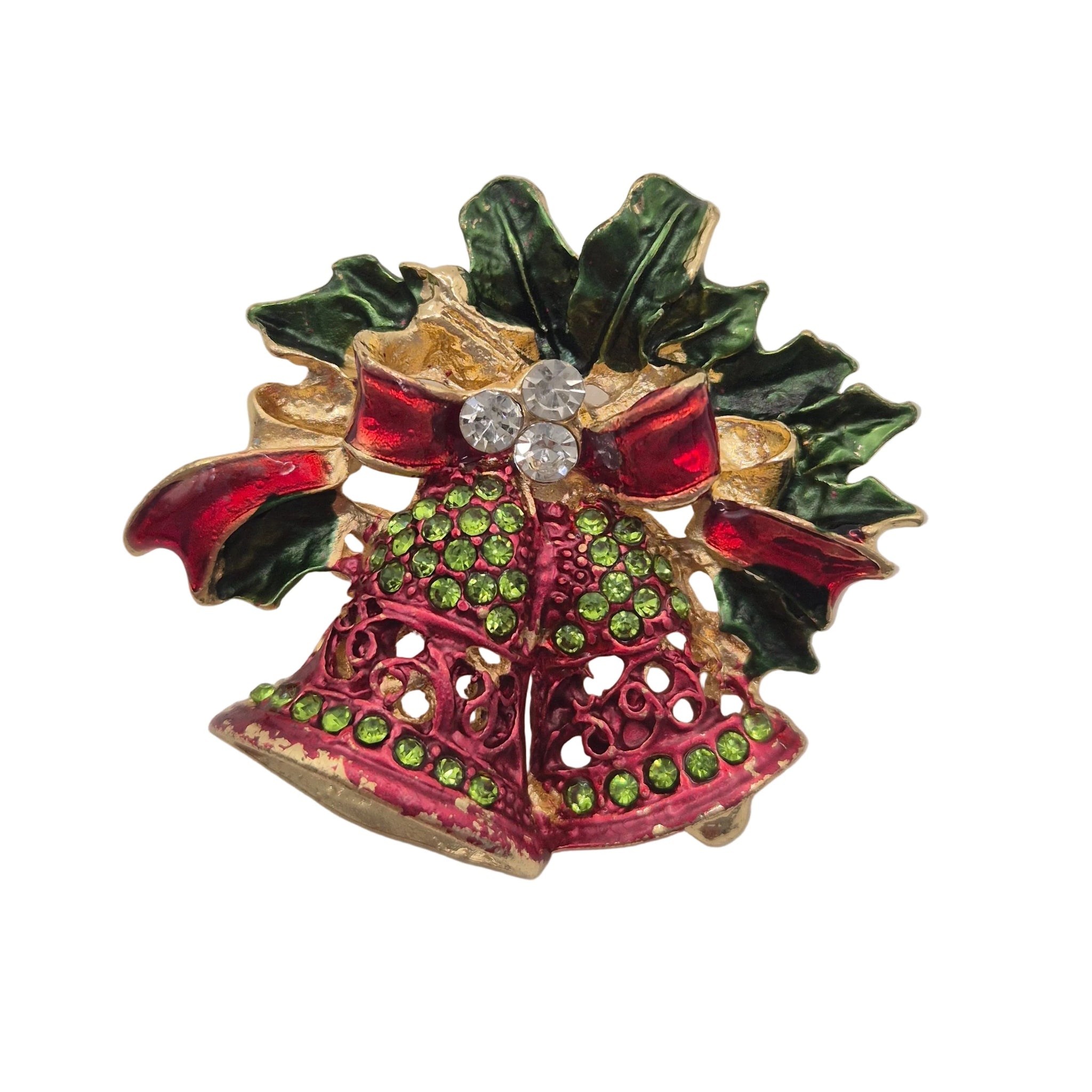 A Christmas-themed brooch featuring two gold-tone bell-shaped ornaments decorated with pink and green enamel, topped with a red bow, green holly leaves, and a clear rhinestone center, shown on a plain white background.
