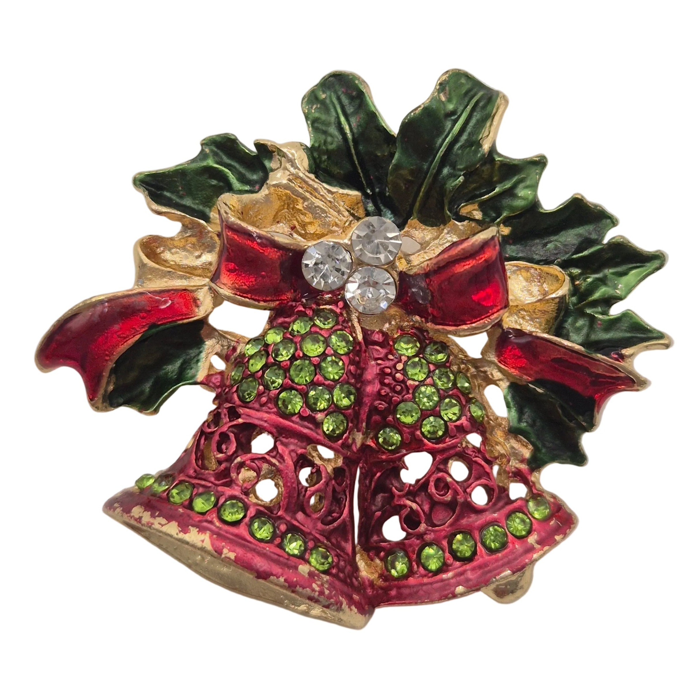 A vintage-style Christmas holly and bell brooch featuring red enamel, green enamel, gold-tone metal, and clear rhinestones on a white background.