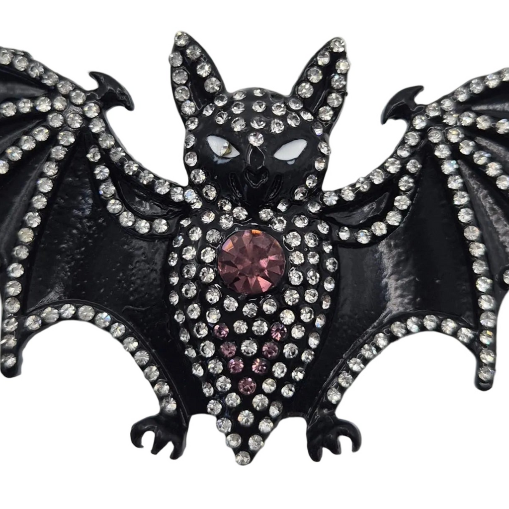 Black bat-shaped brooch embellished with clear rhinestones and a central pink faceted crystal, shown on a plain white background.