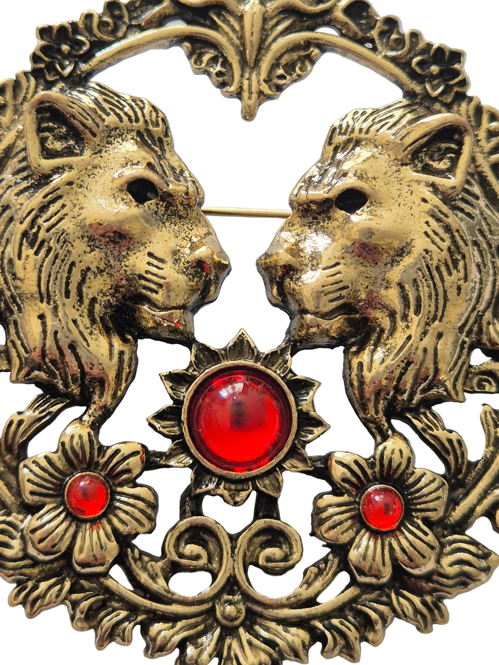 Decorative gold brooch with two lion faces, red gemstones, and floral elements.