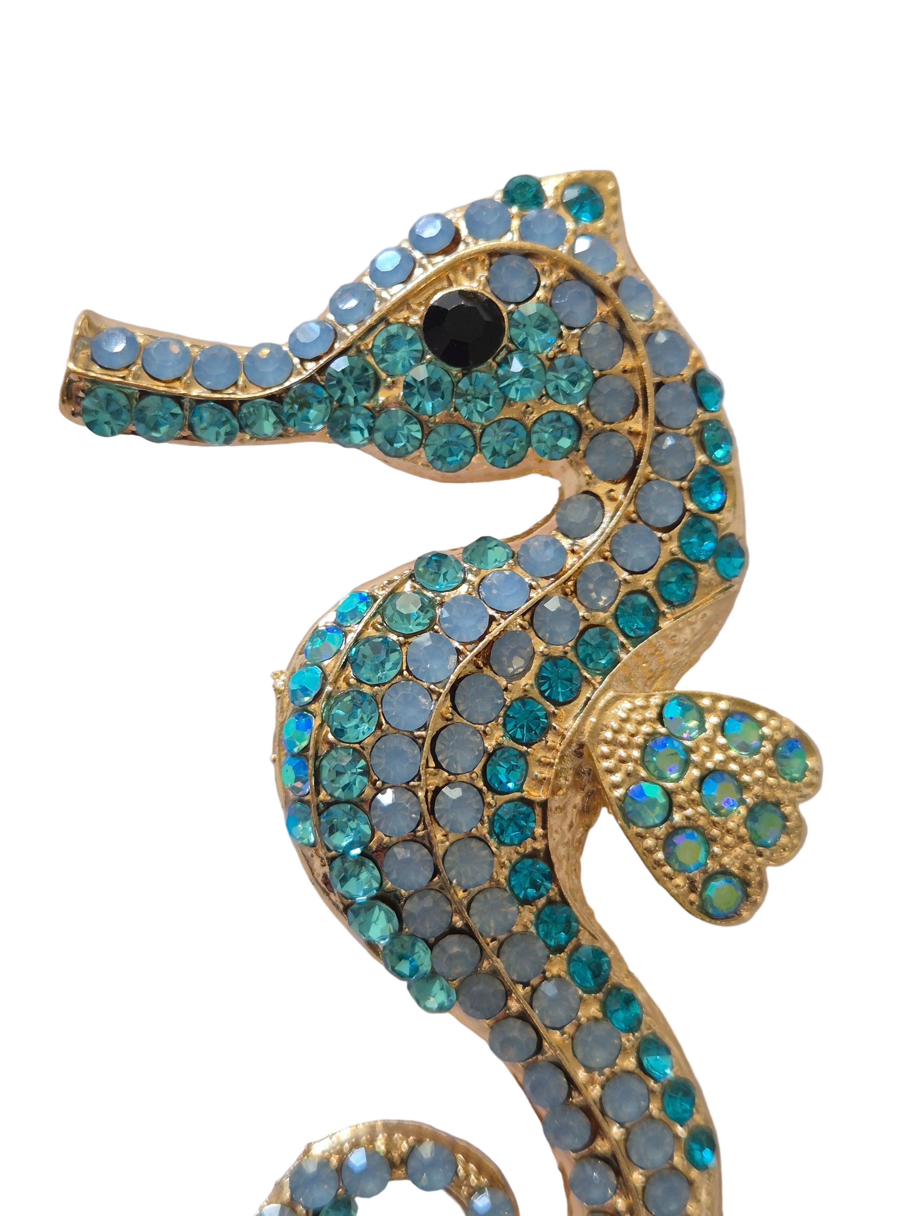 Decorative seahorse brooch with blue and green gemstones on a white background