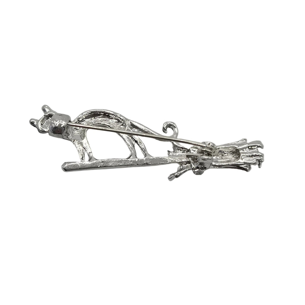 A silver-toned metal brooch featuring a cat standing on a broomstick, displayed against a plain white background.