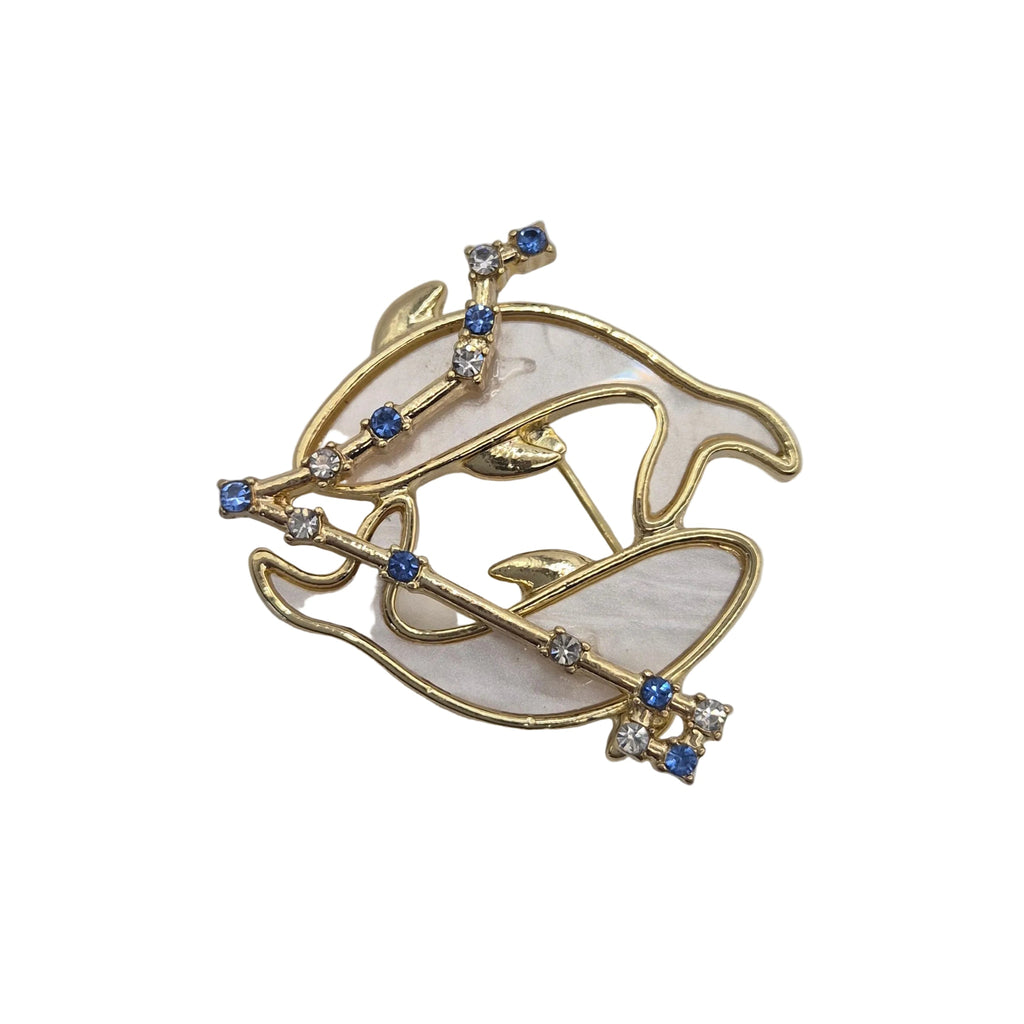 A gold-tone Pisces fish brooch with a milky white mother-of-pearl style inlay and small blue and clear rhinestone accents, shown on a plain white background.