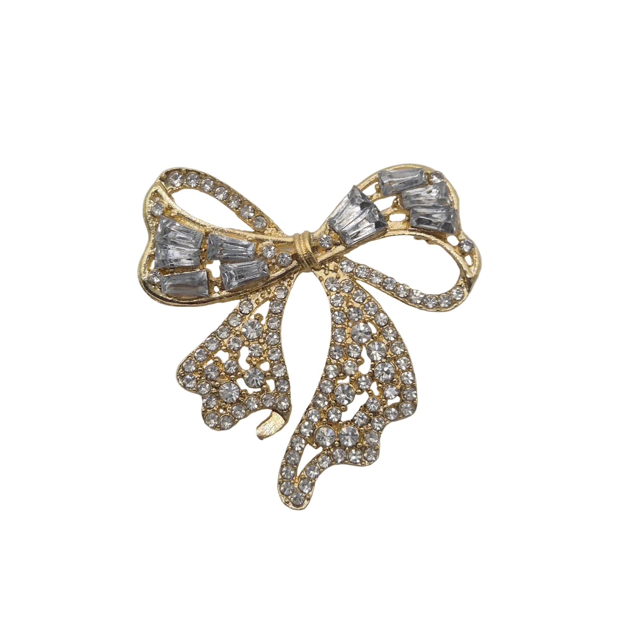 A gold bow-shaped brooch embellished with clear baguette and round crystals, photographed on a plain white background.