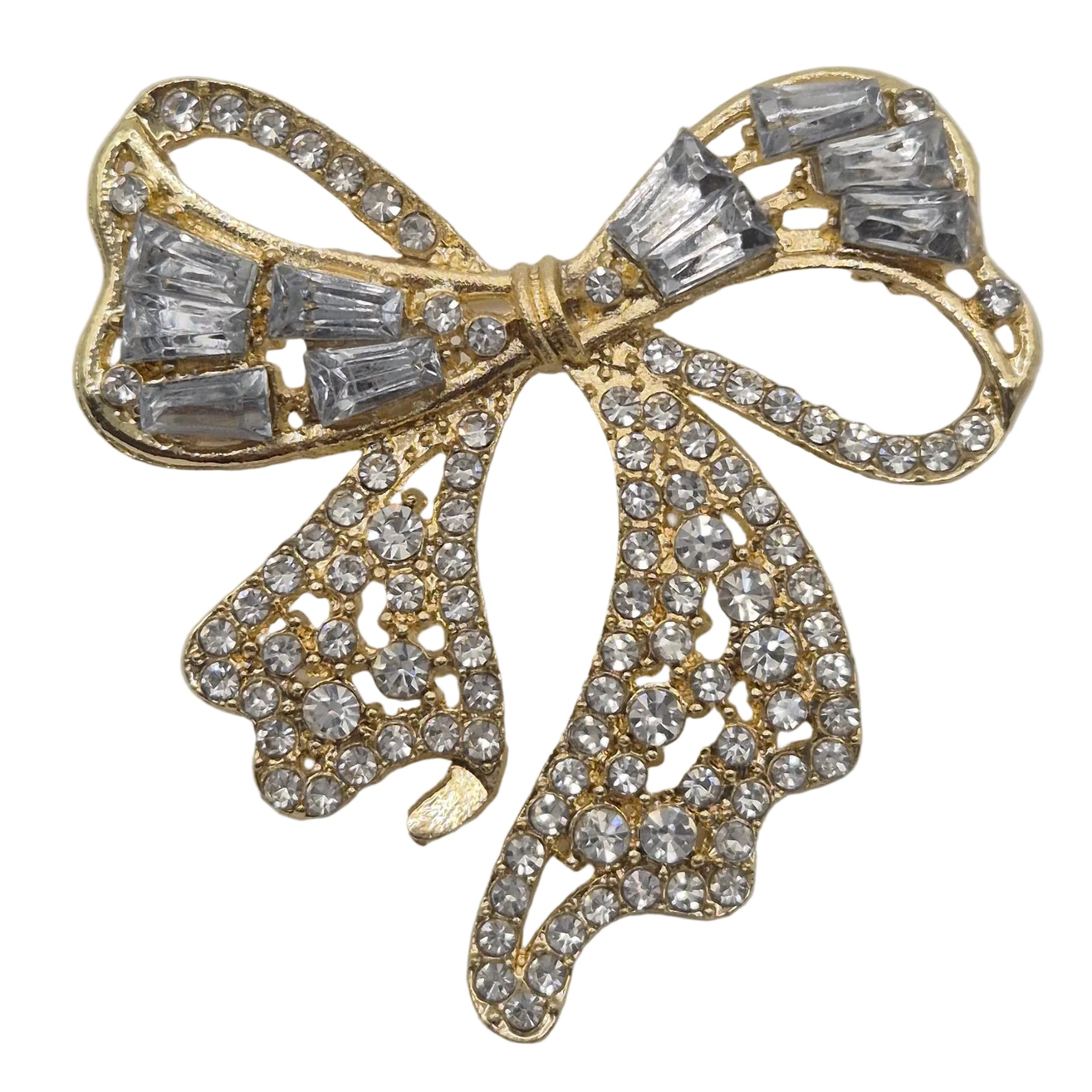 A gold bow-shaped brooch embellished with clear baguette and round crystals, photographed on a plain white background.