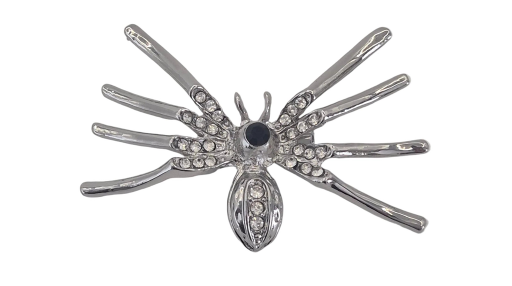 A silver spider brooch embellished with clear rhinestones and a central dark blue gemstone, shown on a plain white background.