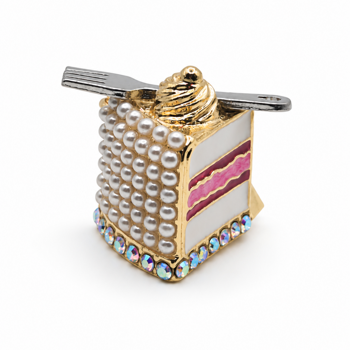 A novelty cake slice brooch with a gold-tone metal base, detailed with faux pearls, pink and white striped enameled layers, iridescent rhinestones, and a small silver fork resting across the top, shown on a plain white background.