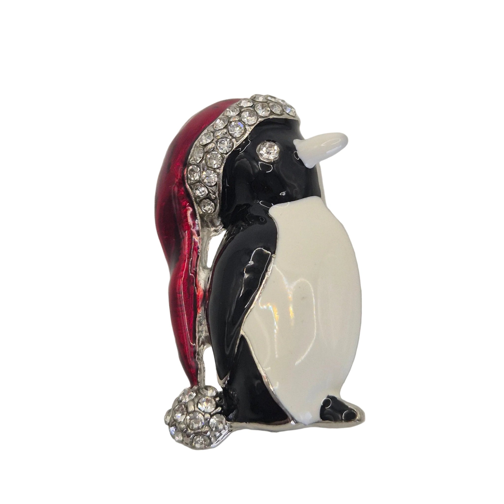 A penguin-shaped brooch with a glossy black and white body, wearing a red hat embellished with clear rhinestones, photographed on a plain white background.