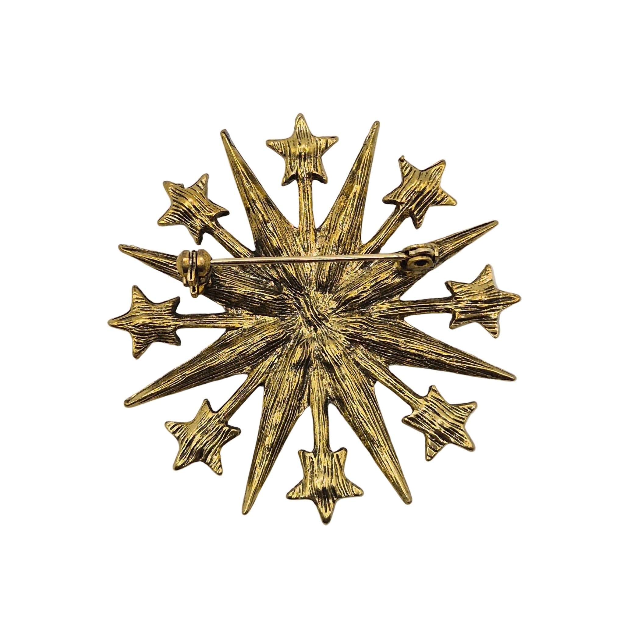 A gold-toned starburst brooch with textured rays and multiple small star points, photographed on a plain white background.