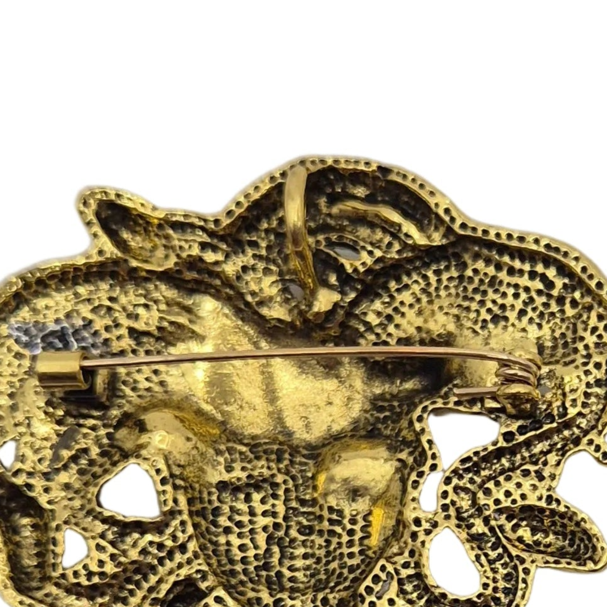 Close-up of a gold-tone textured brooch with a pin clasp, showing an intricate hammered and dotted metallic surface on a plain white background.