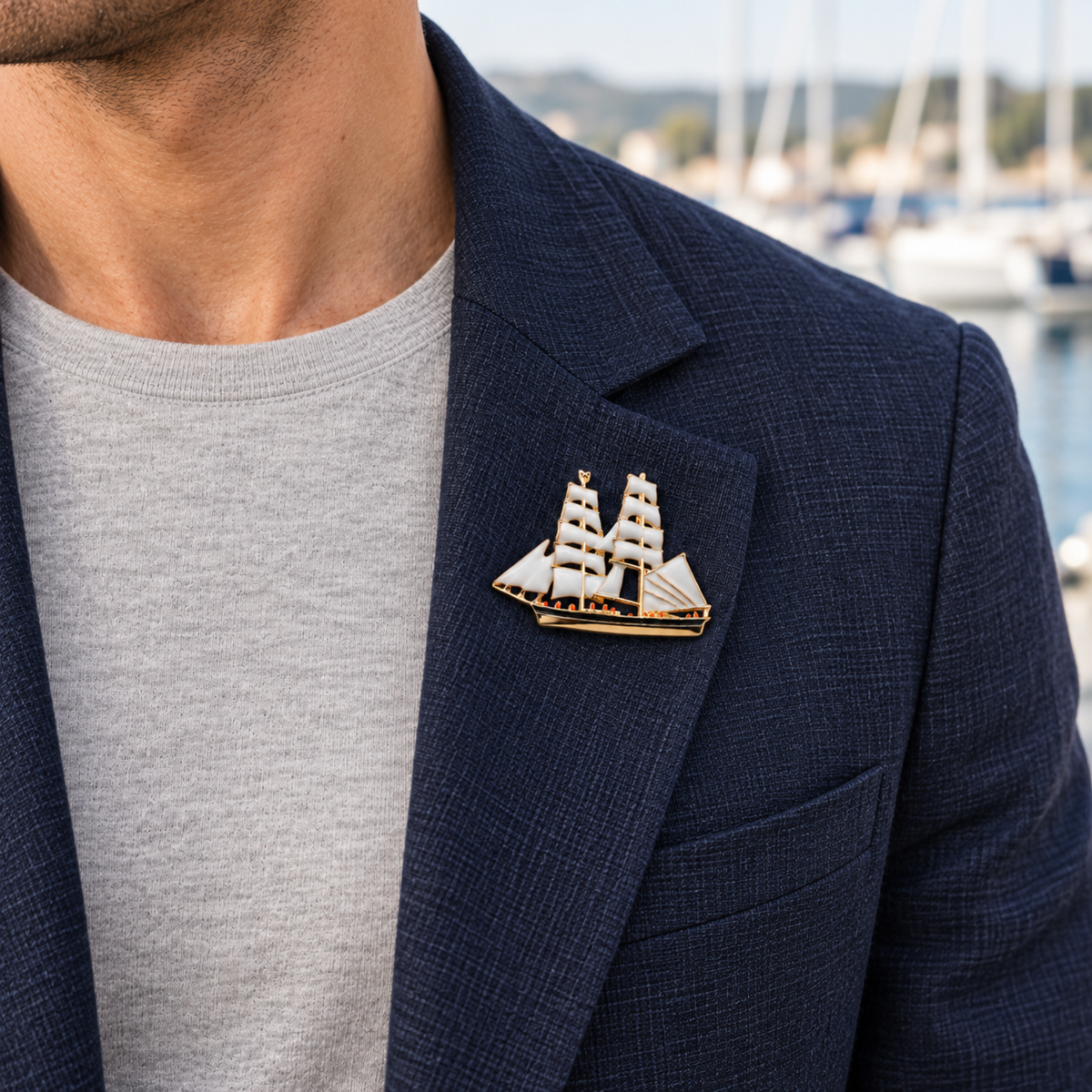 A close-up of a man wearing a navy blazer over a light gray t-shirt, featuring a detailed gold and white sailing ship lapel pin on his chest.