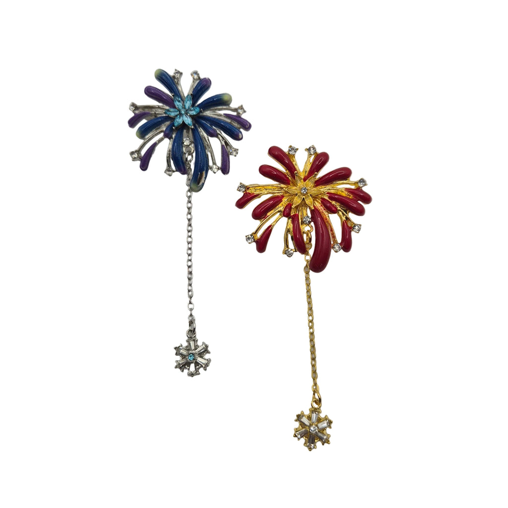 Two vintage-style firework brooches with dangling chains and snowflake charms, one in blue and purple enamel with silver-tone metal, and the other in red and gold enamel with silver-tone metal, shown on a plain white background.