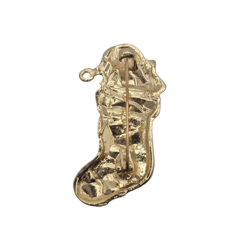 A small gold Christmas stocking-shaped brooch or charm with a visible pin mechanism, photographed on a plain white background.