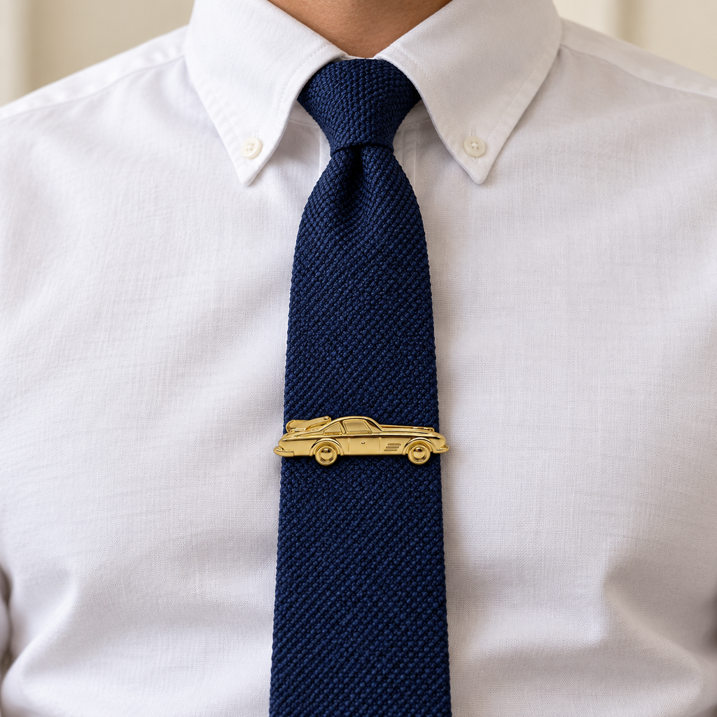A close-up of a man wearing a white button-down shirt and a textured navy blue tie, featuring a gold car-shaped tie clip at the center.