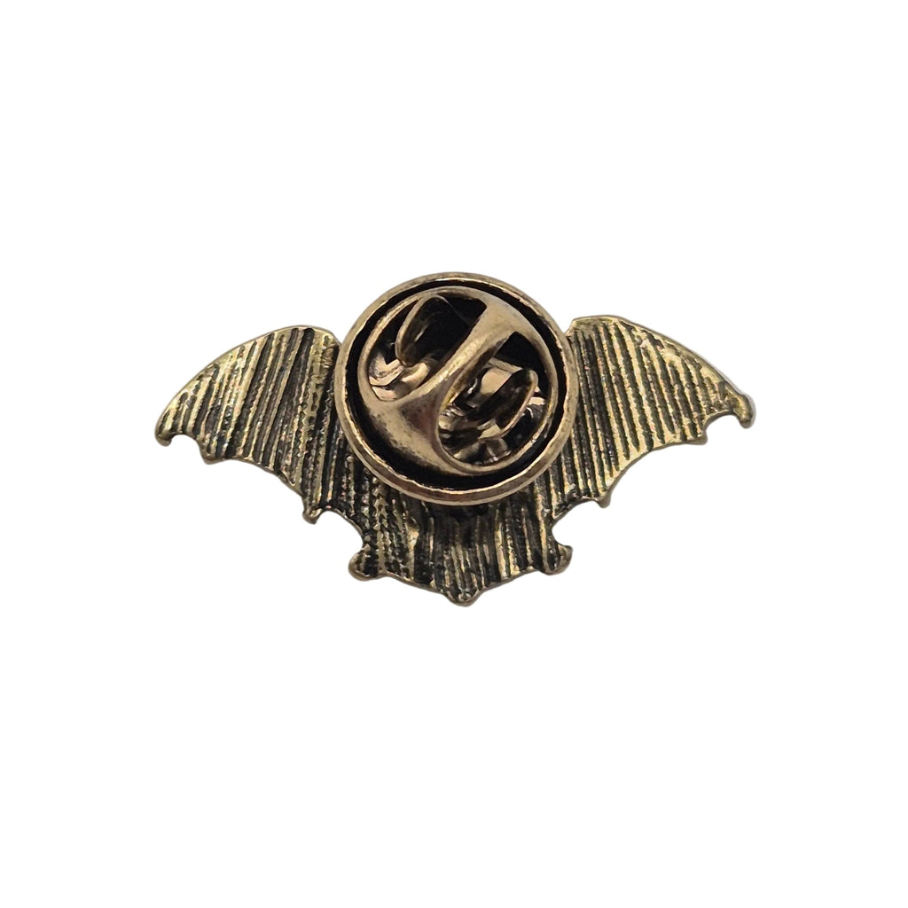 A small vintage-style metal pin shaped like a bat with spread wings and a circular center, shown on a plain white background.