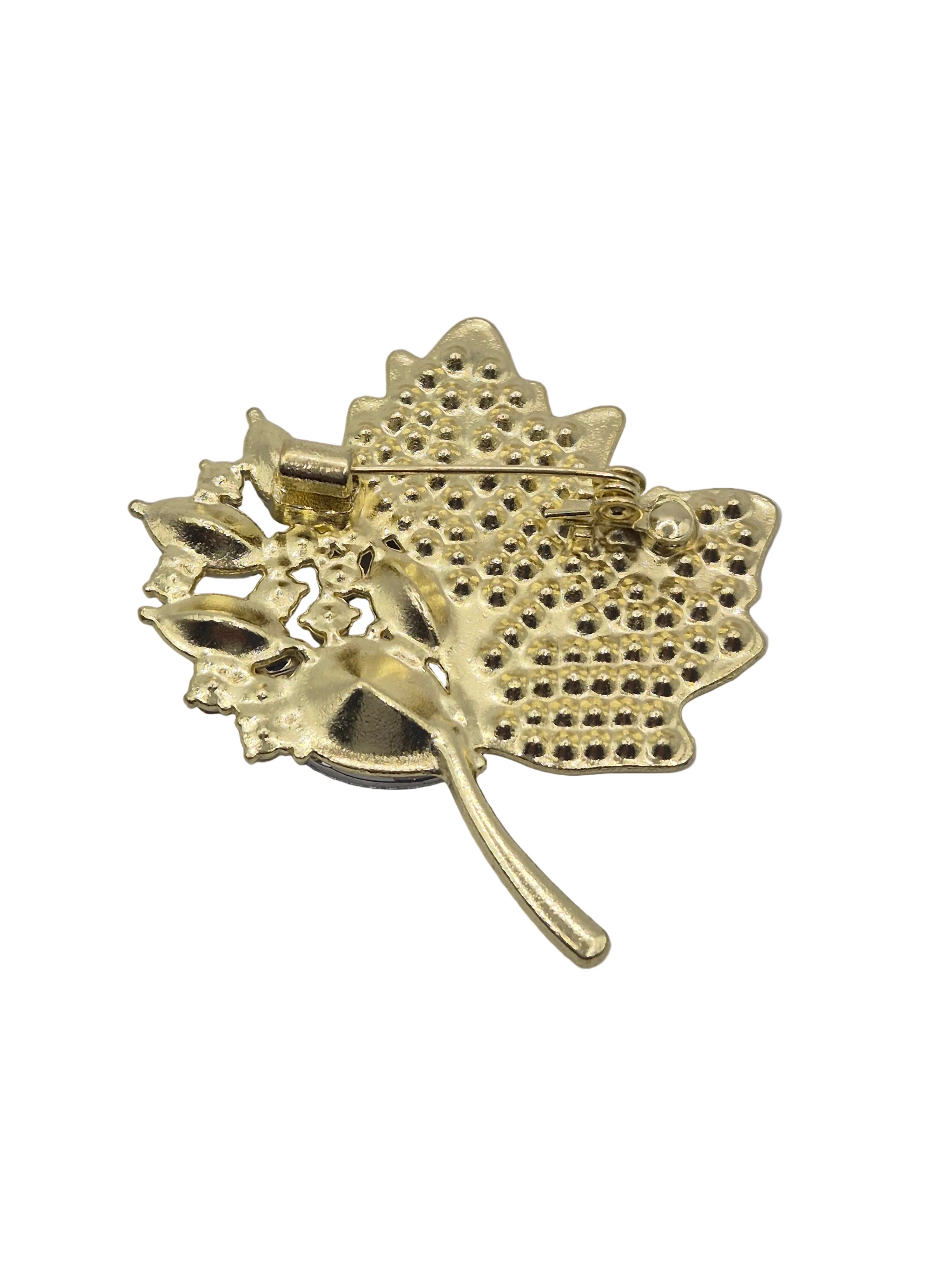 A gold-toned metal leaf-shaped brooch with a textured, perforated pattern and a pin clasp visible on the reverse side, shown against a plain white background.
